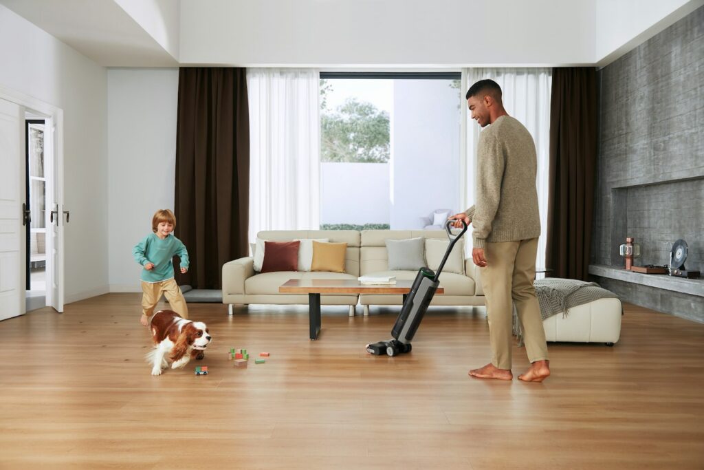 Parent vacuuming a living room floor while a child and a dog play nearby, a home that suits weekly cleaning