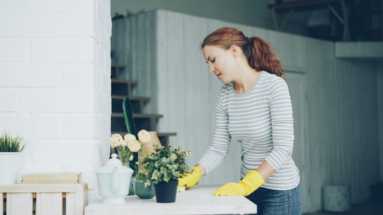 Cleaner in yellow gloves wiping down a table during a recurring house cleaning visit